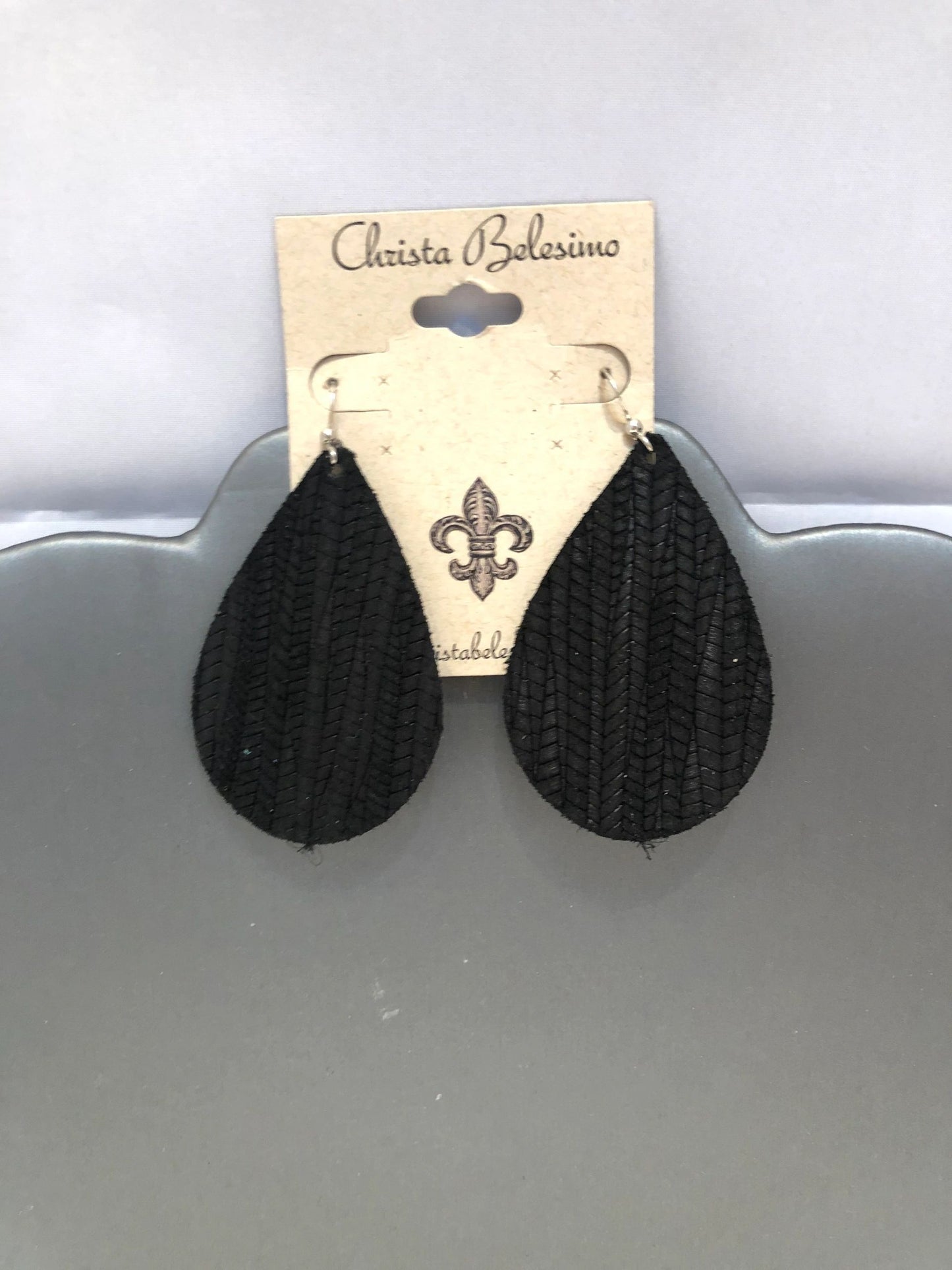 A pair of black textured vegan leather earrings displayed on a card with the brand name 'Christa Bellesima'.