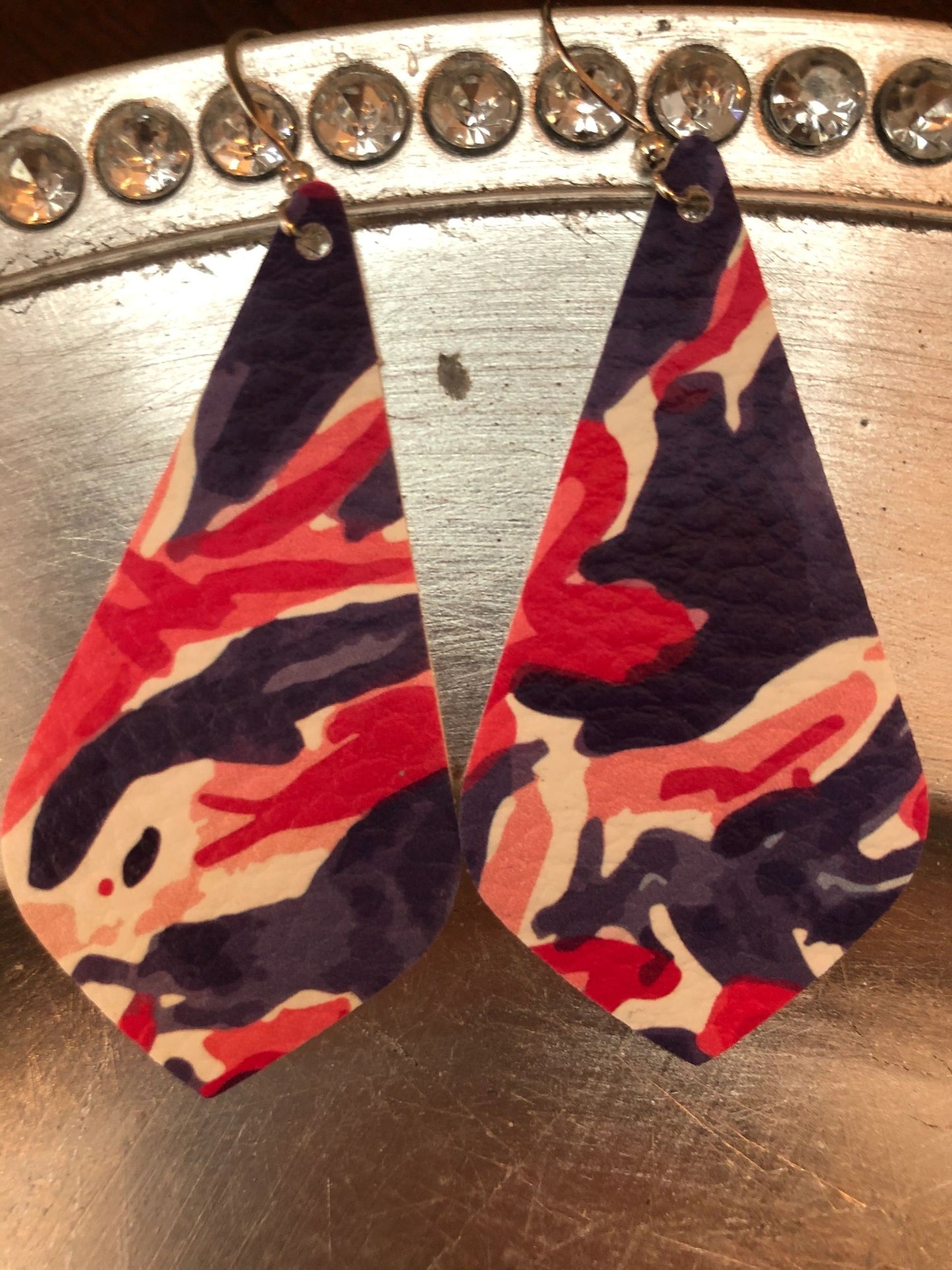 A pair of pink, blue, and purple leather earrings displayed on a reflective surface.