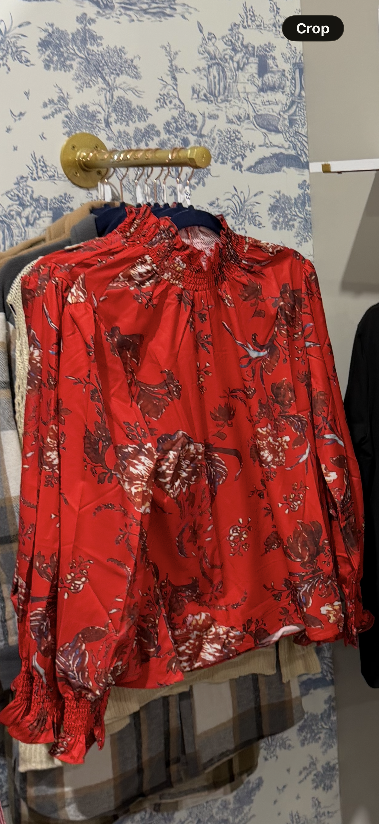 Red floral blouse on a hanger against a patterned wall.