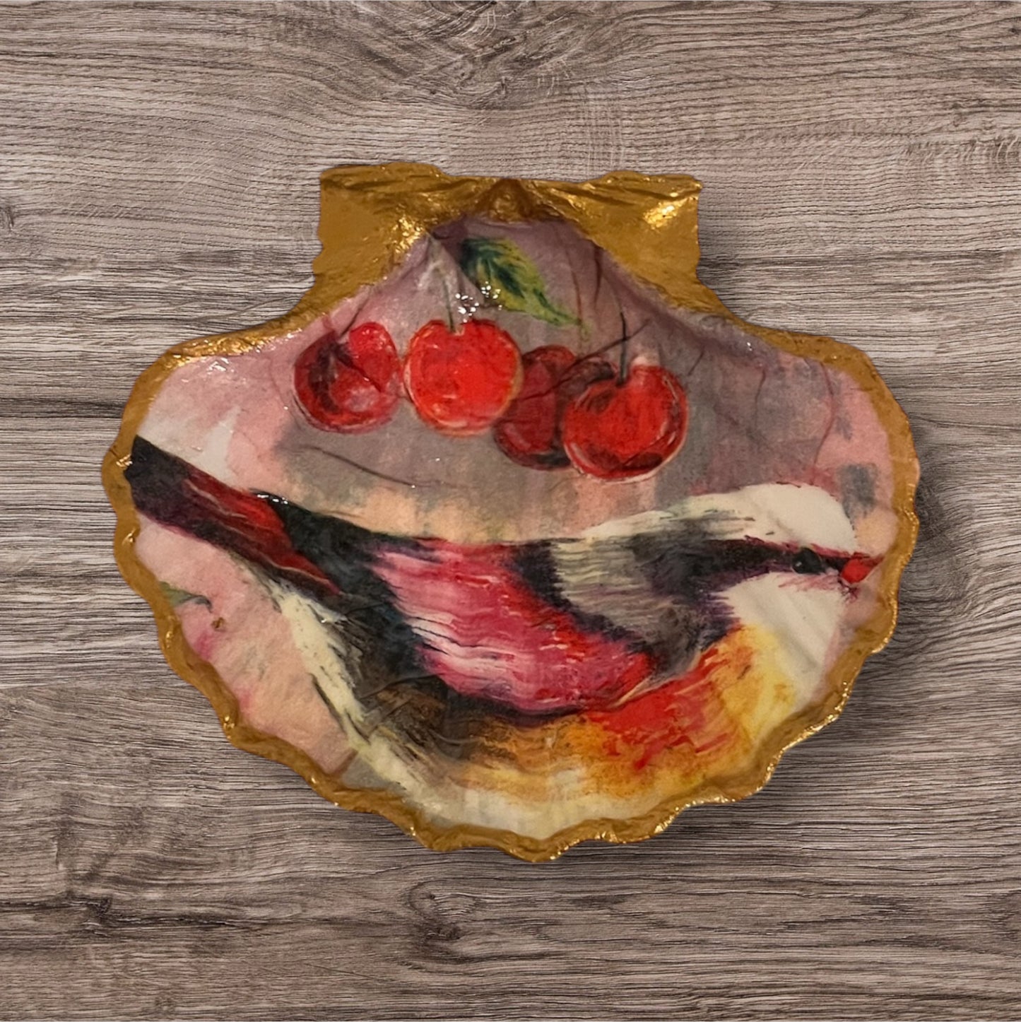 A decorative scallop shell with a painted red bird and cherries, with a gold edge.