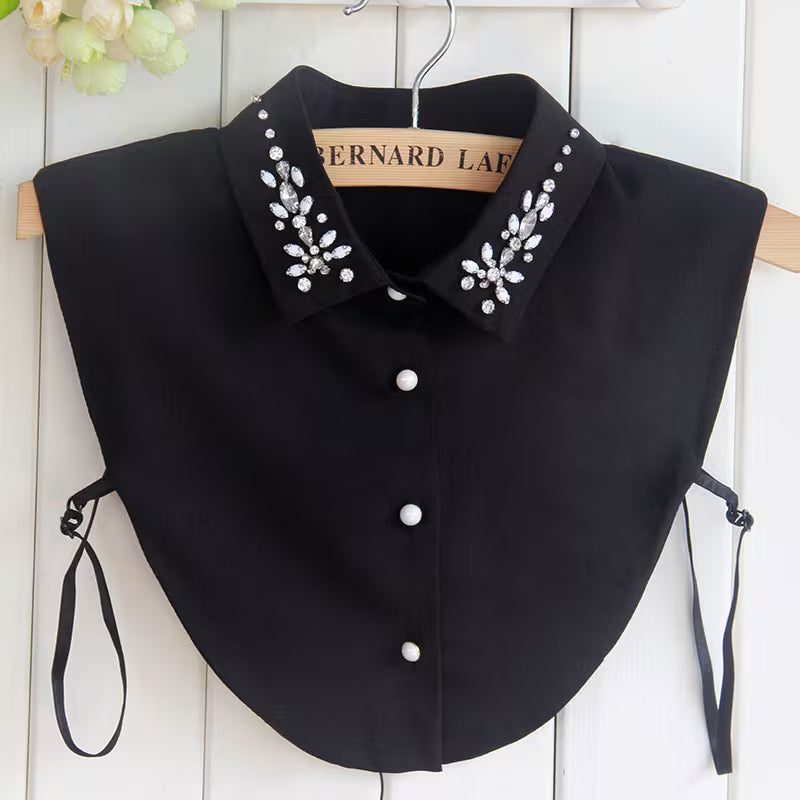 Black collar with decorative buttons and embellishments on a hanger against a white wooden panel background.