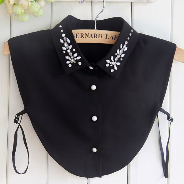 Black collar with decorative buttons and embellishments on a hanger against a white wooden panel background.