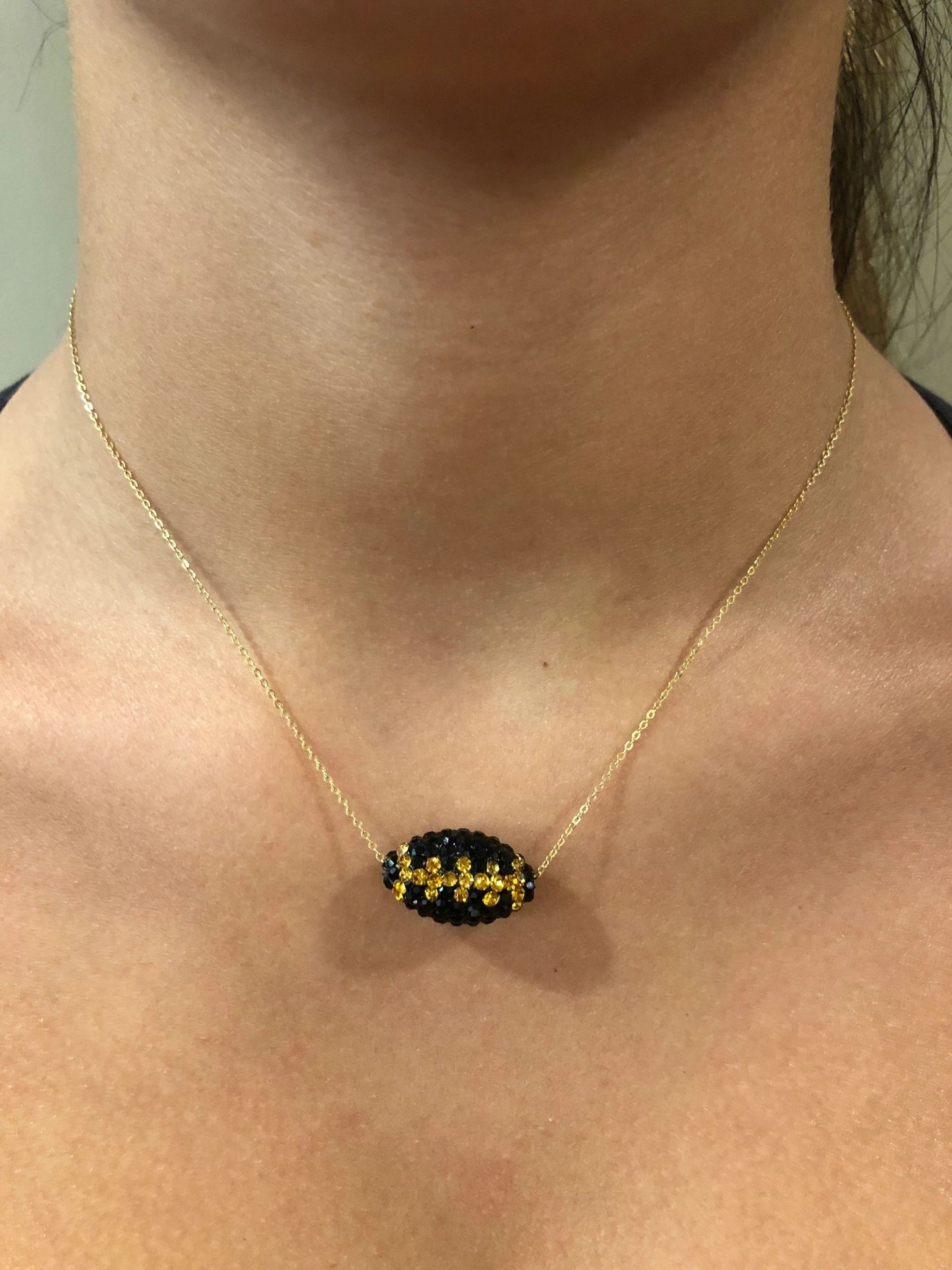 A gold chain necklace with a black and gold football-shaped pendant representing the New Orleans Saints.