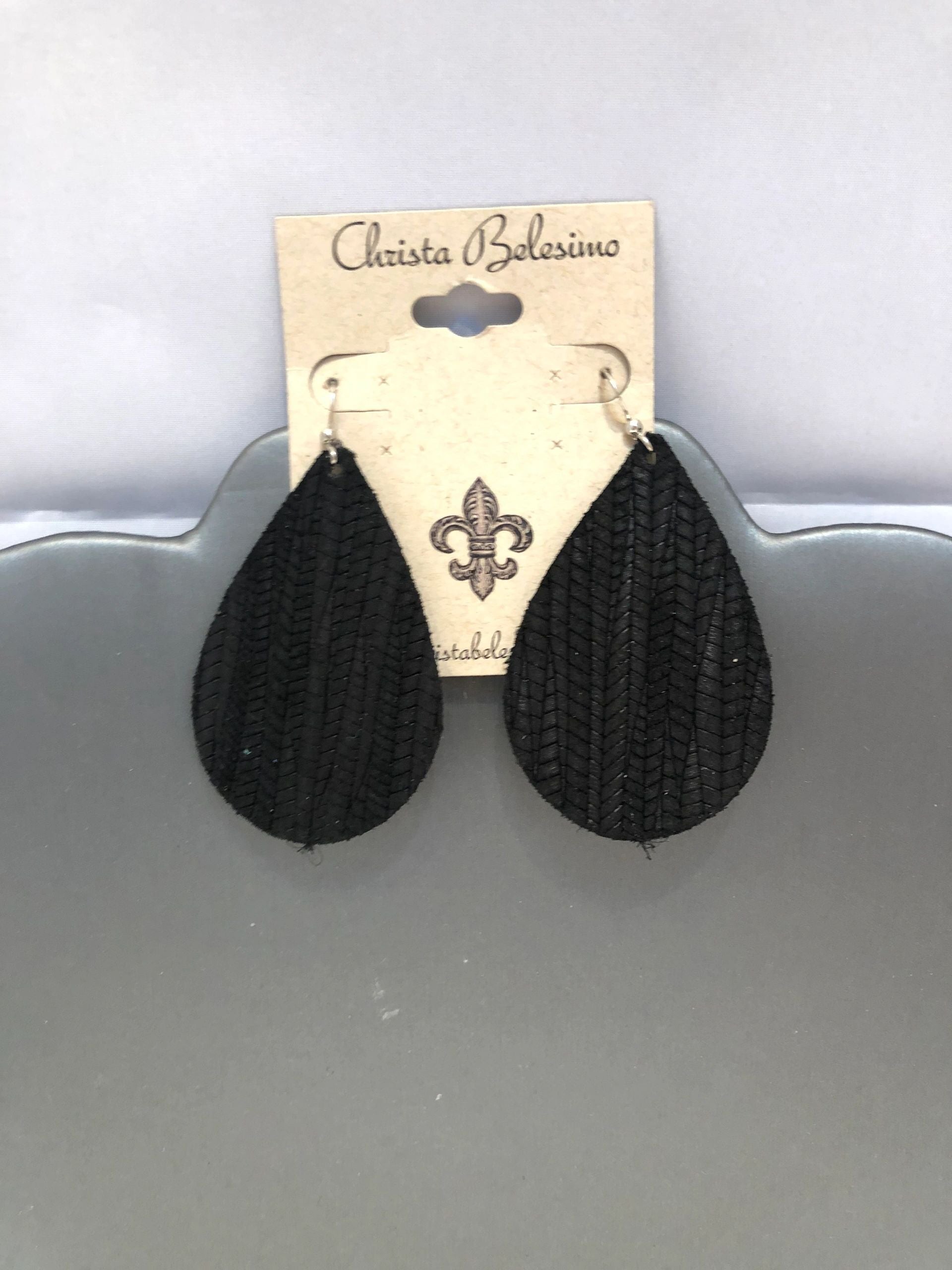 A pair of black textured vegan leather earrings displayed on a card with the brand name 'Christa Bellesima'.
