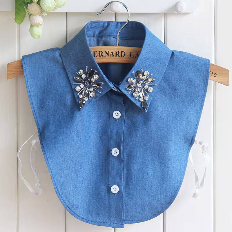 Blue denim collar with decorative buttons and embellishments on a hanger against a white wooden panel background.