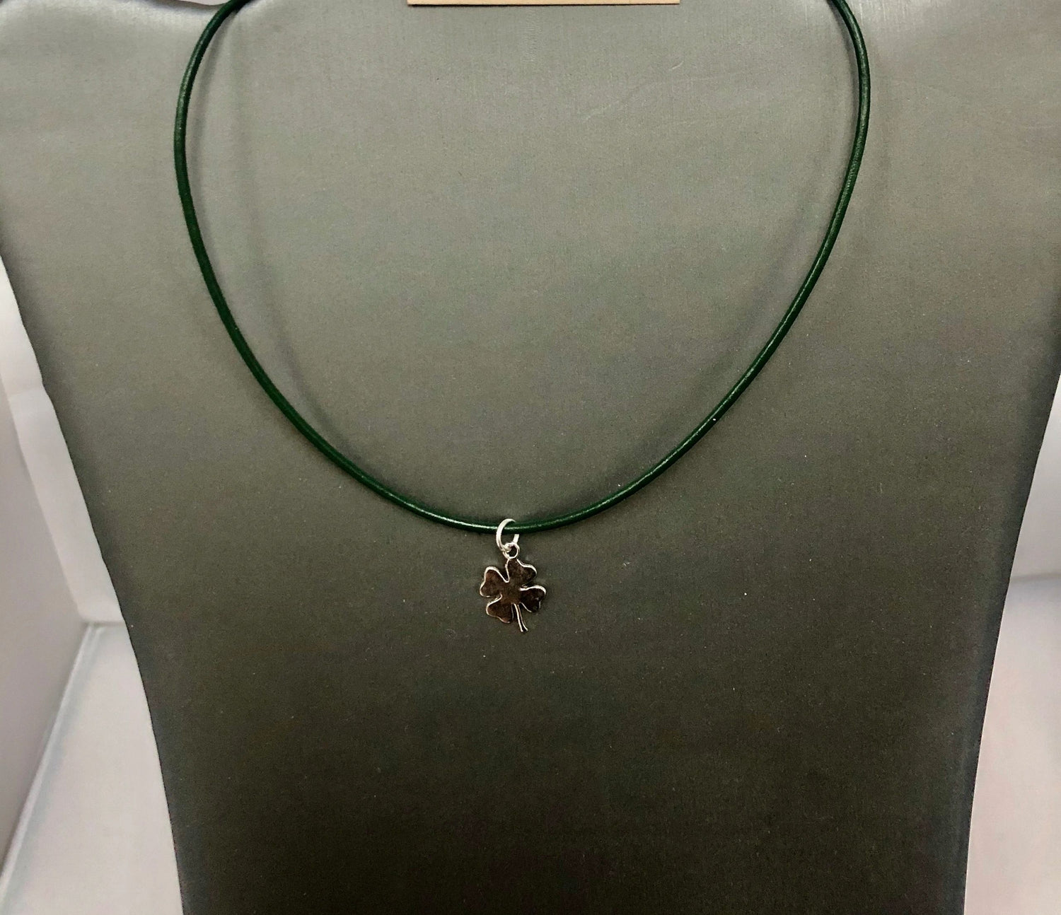 A green leather cord necklace with a silver clover shamrock pendant on display mannequin.