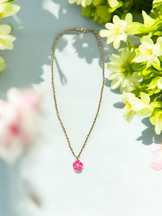 A white enamel flower necklace with a pink center on a gold-filled chain, displayed against a floral background.