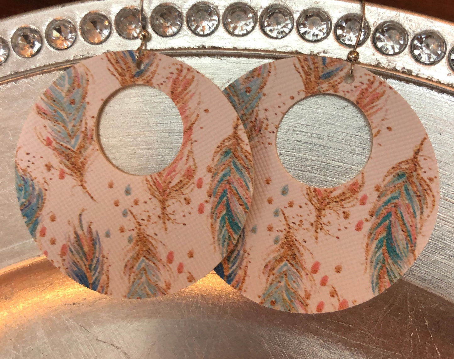 A pair of round vegan earrings with a feather print design, displayed on a metal surface.
