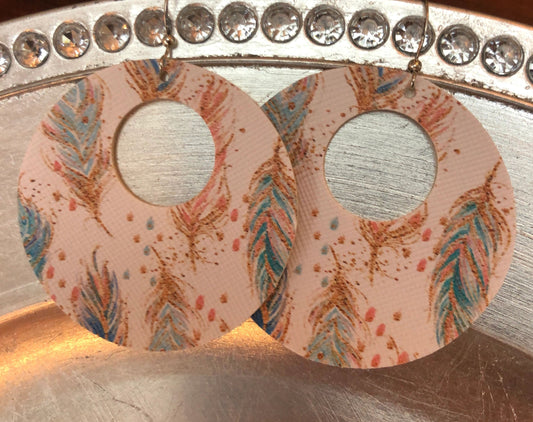 A pair of round vegan earrings with a feather print design, displayed on a metal surface.