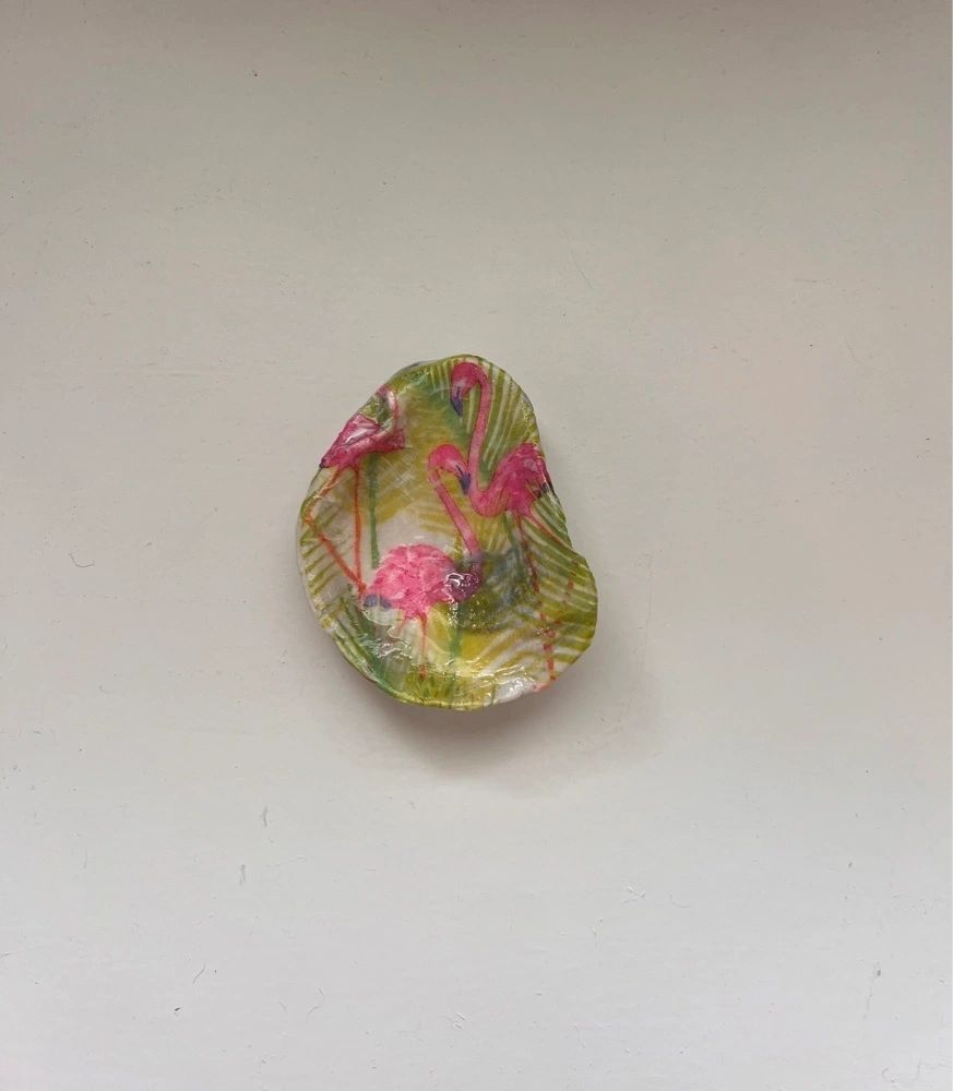 A decoupage oyster shell with pink flamingos pattern used as a trinket holder, mounted on a wall.