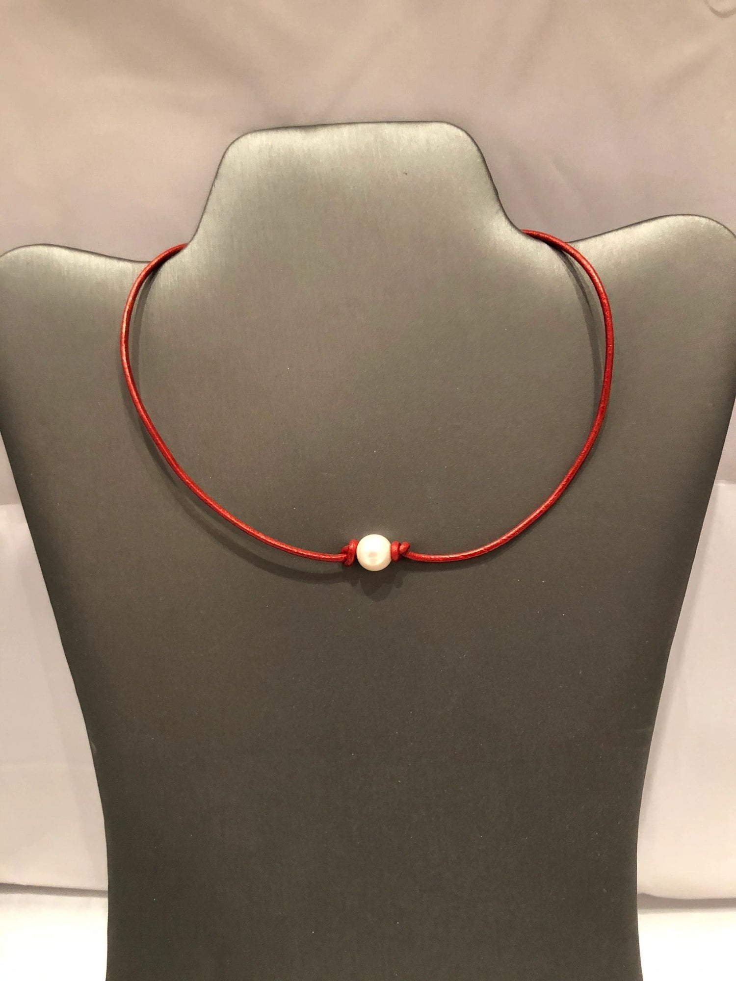 A red leather necklace with a freshwater pearl on a silver lobster clasp closure, displayed on a mannequin bust.