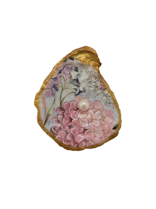 An oyster shell with gold painted trim and a pearl in the center, decorated with a floral pattern in pink and purple colors.