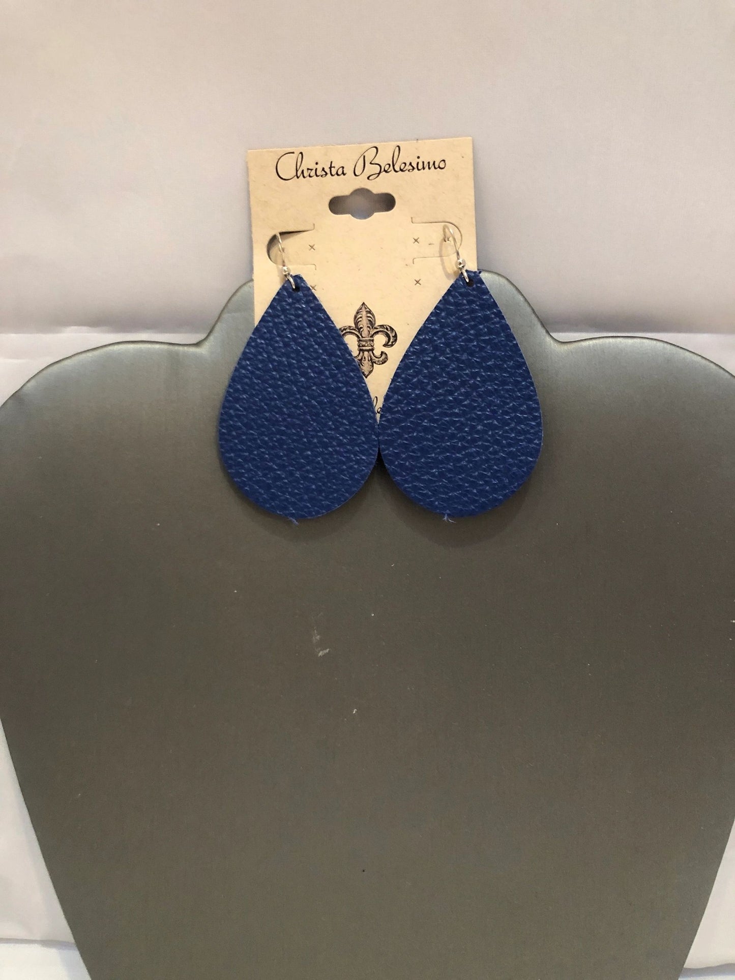 A pair of navy blue leather earrings displayed on a silver-colored earring stand with the brand name 'Charlotte Bella' tagged on the top.