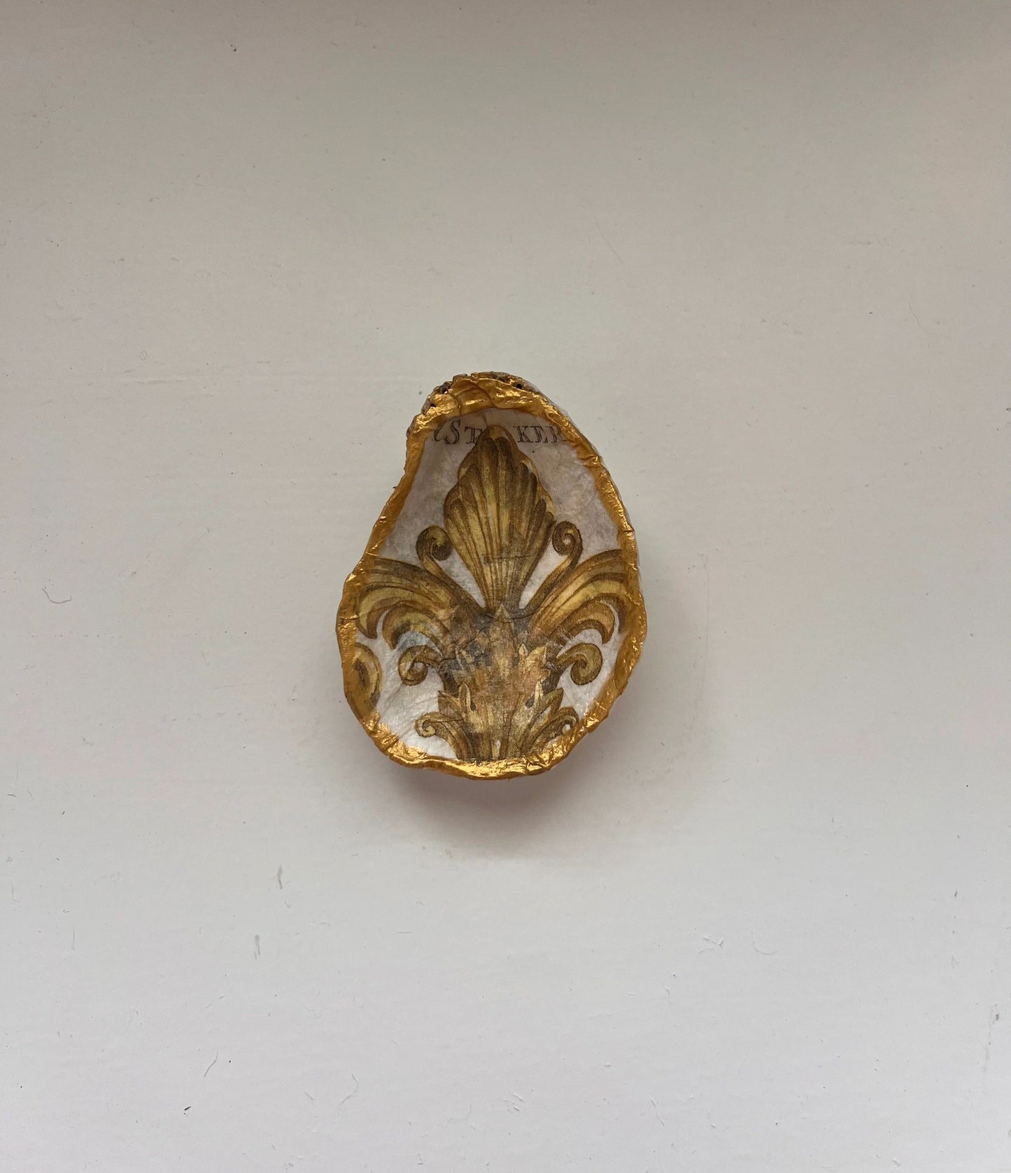 A gold-colored oyster shell-shaped trinket holder mounted on a wall.