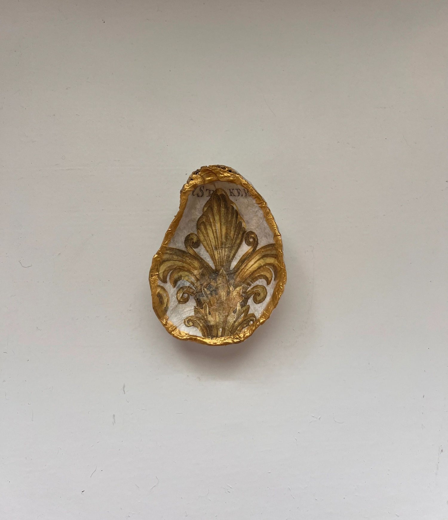 A gold-colored oyster shell-shaped trinket holder mounted on a wall.