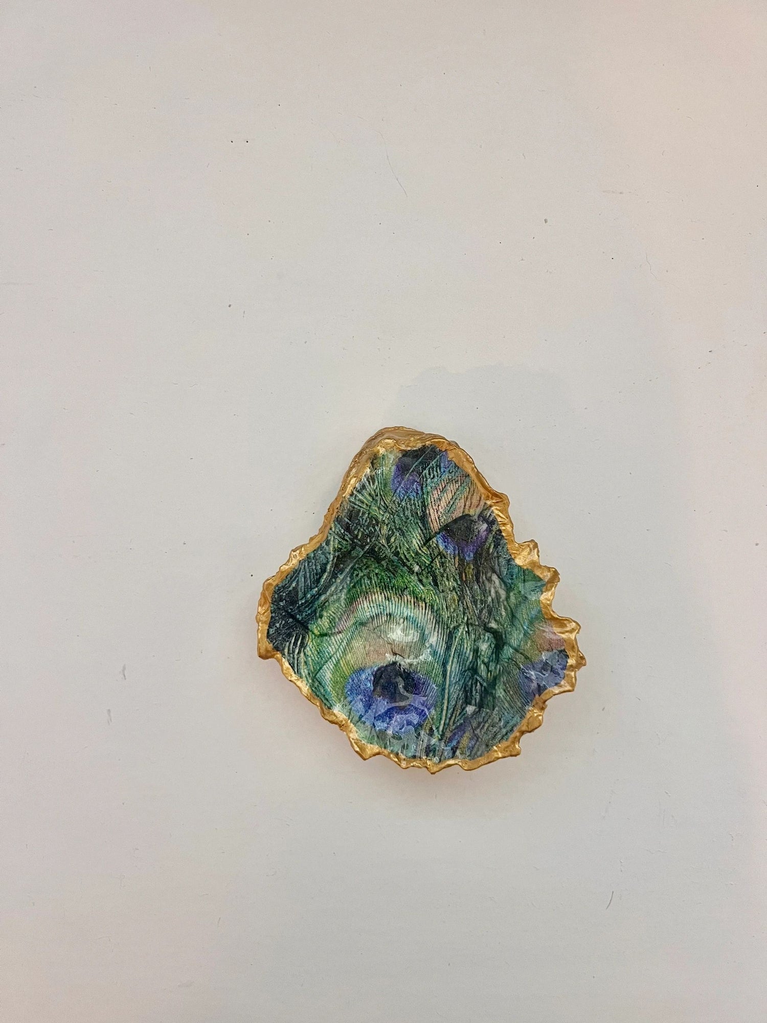 A gold-trimmed oyster shell trinket holder with a peacock feather pattern on the bottom right.