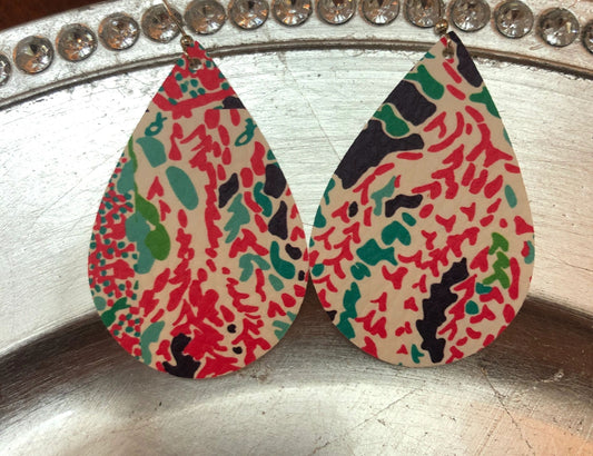 A pair of pink and blue floral patterned vegan earrings displayed on a metal surface.
