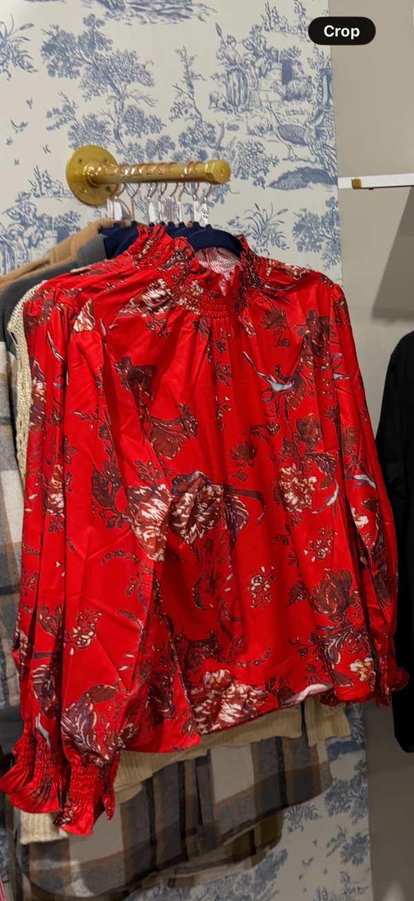 Red floral blouse on a hanger against a patterned wall.