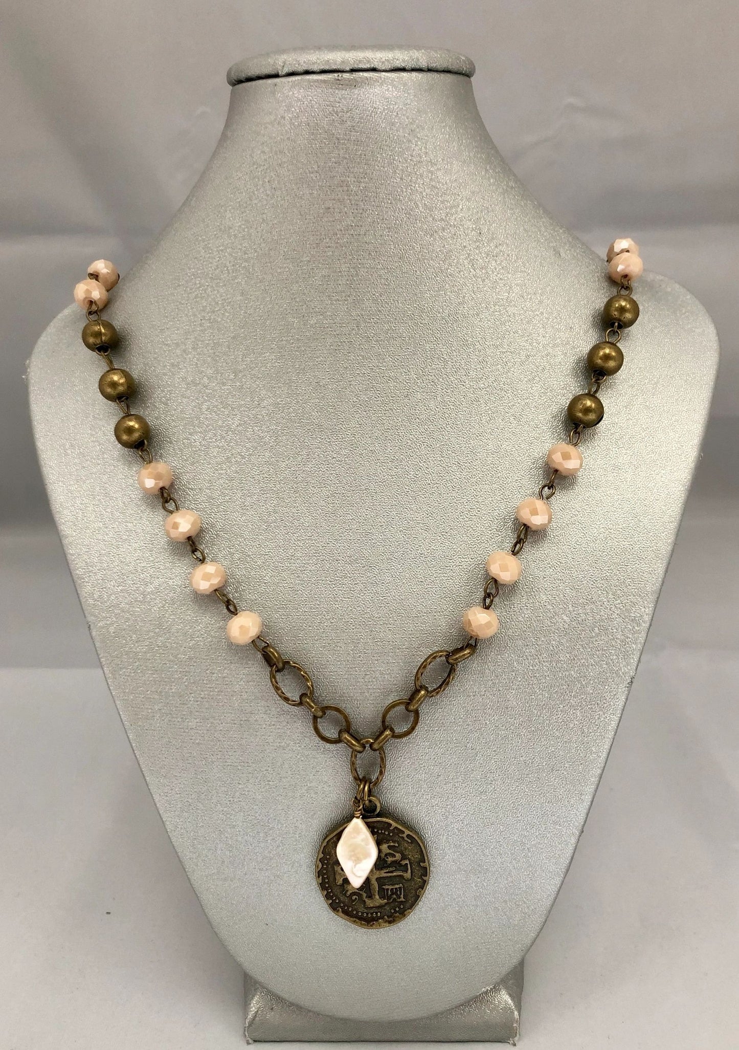 A beaded necklace with a brass-looking coin pendant, displayed on a mannequin bust.