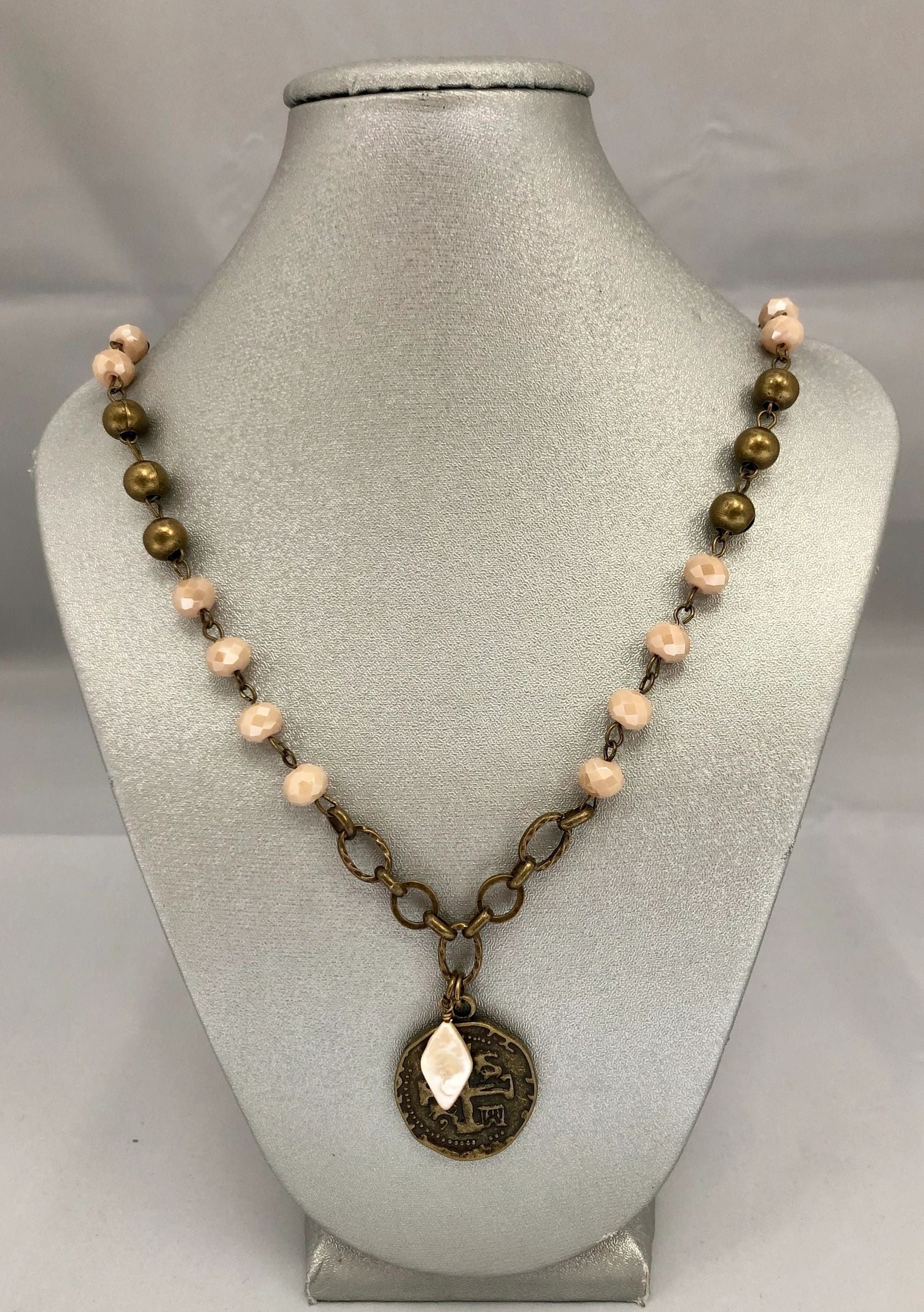 A beaded necklace with a brass-looking coin pendant, displayed on a mannequin bust.