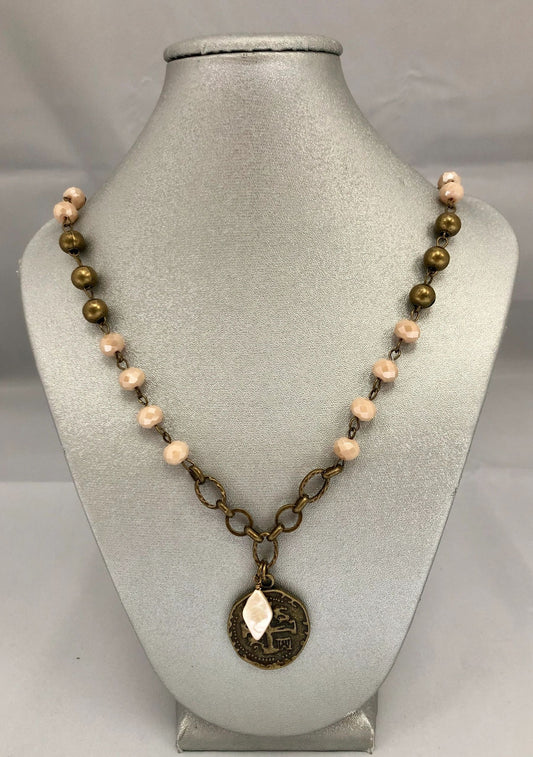A beaded necklace with a brass-looking coin pendant, displayed on a mannequin bust.