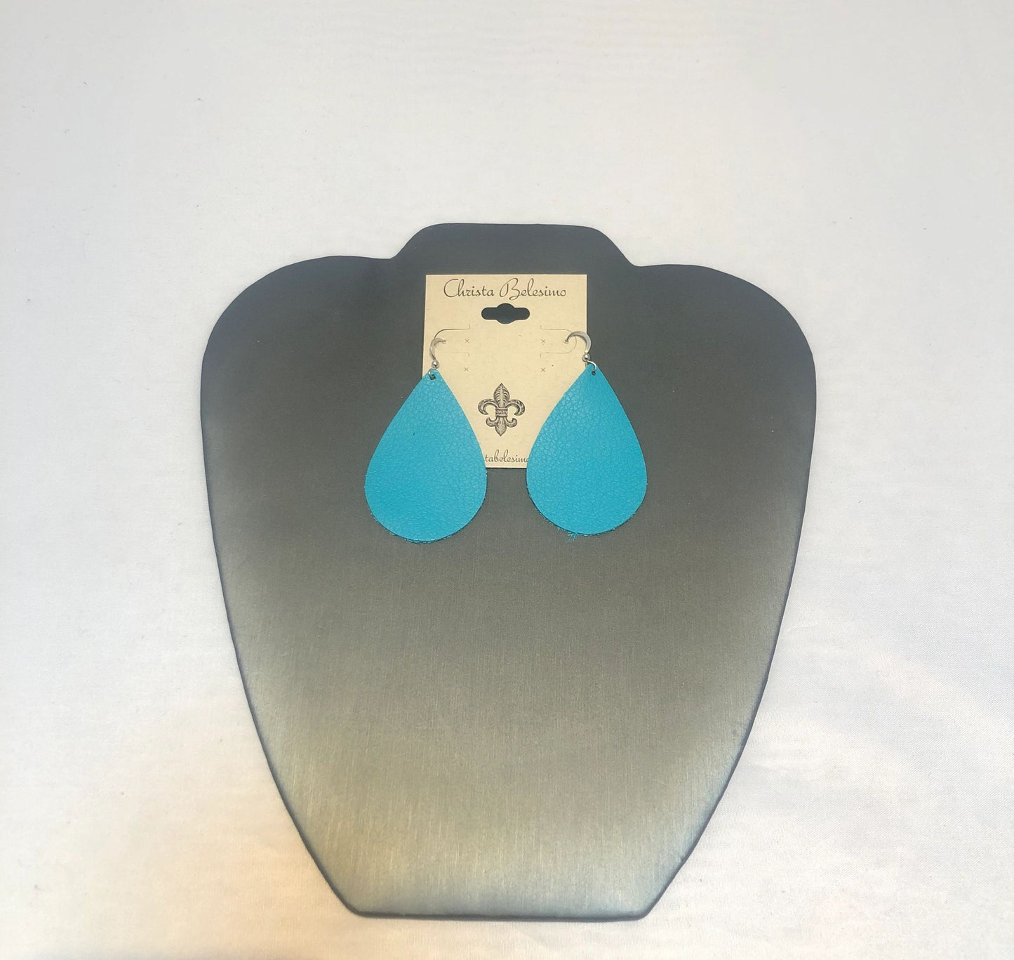 Turquoise leather earrings with silver hooks, displayed on a silver earring stand with a brand tag attached.