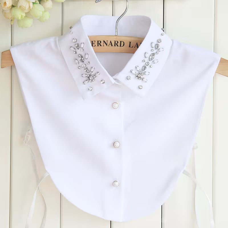 White blouse with decorative collar and buttons on a wooden hanger against a light wooden background.