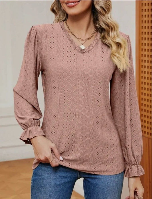 A woman wearing a long sleeve blush pink top with eyelets and elastic at the wrists, paired with blue jeans.