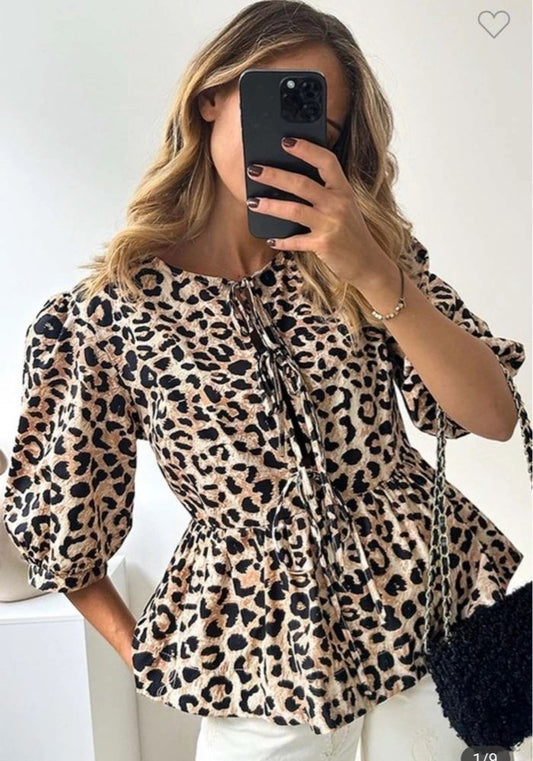 A woman wearing a leopard print tie-front top with puff sleeves, taking a mirror selfie.