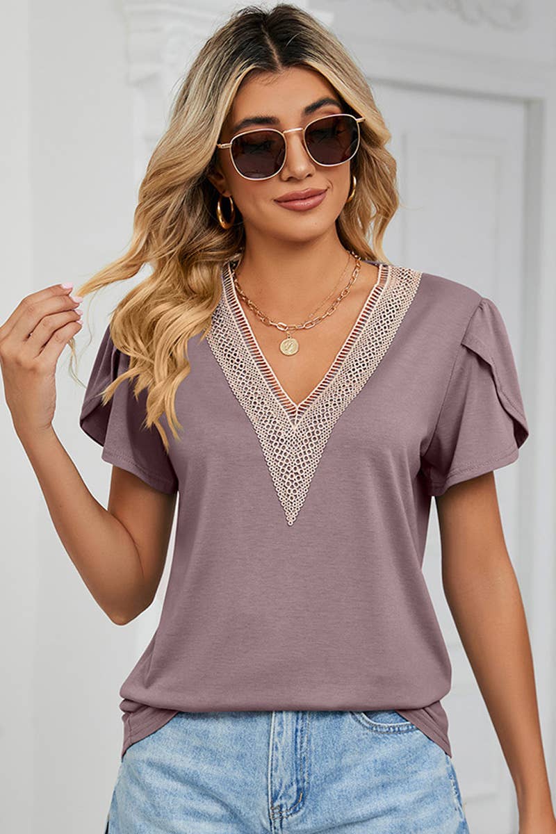 A woman wearing a beige lace V-neck ruffle short-sleeve top and blue jeans.