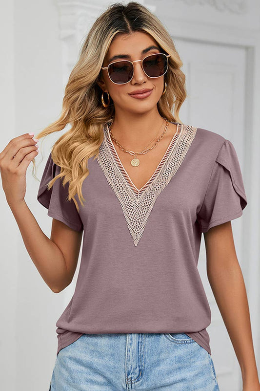 A woman wearing a beige lace V-neck ruffle short-sleeve top and blue jeans.