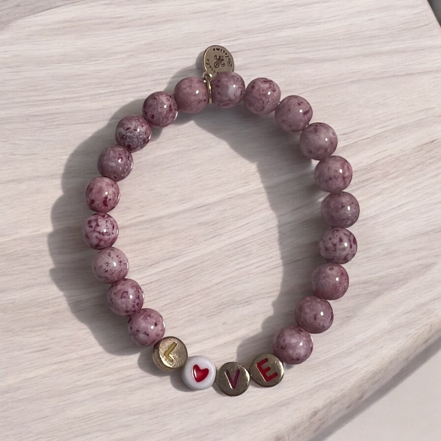 A pink beaded stretch bracelet with the word 'love' and a heart symbol on a wooden surface.