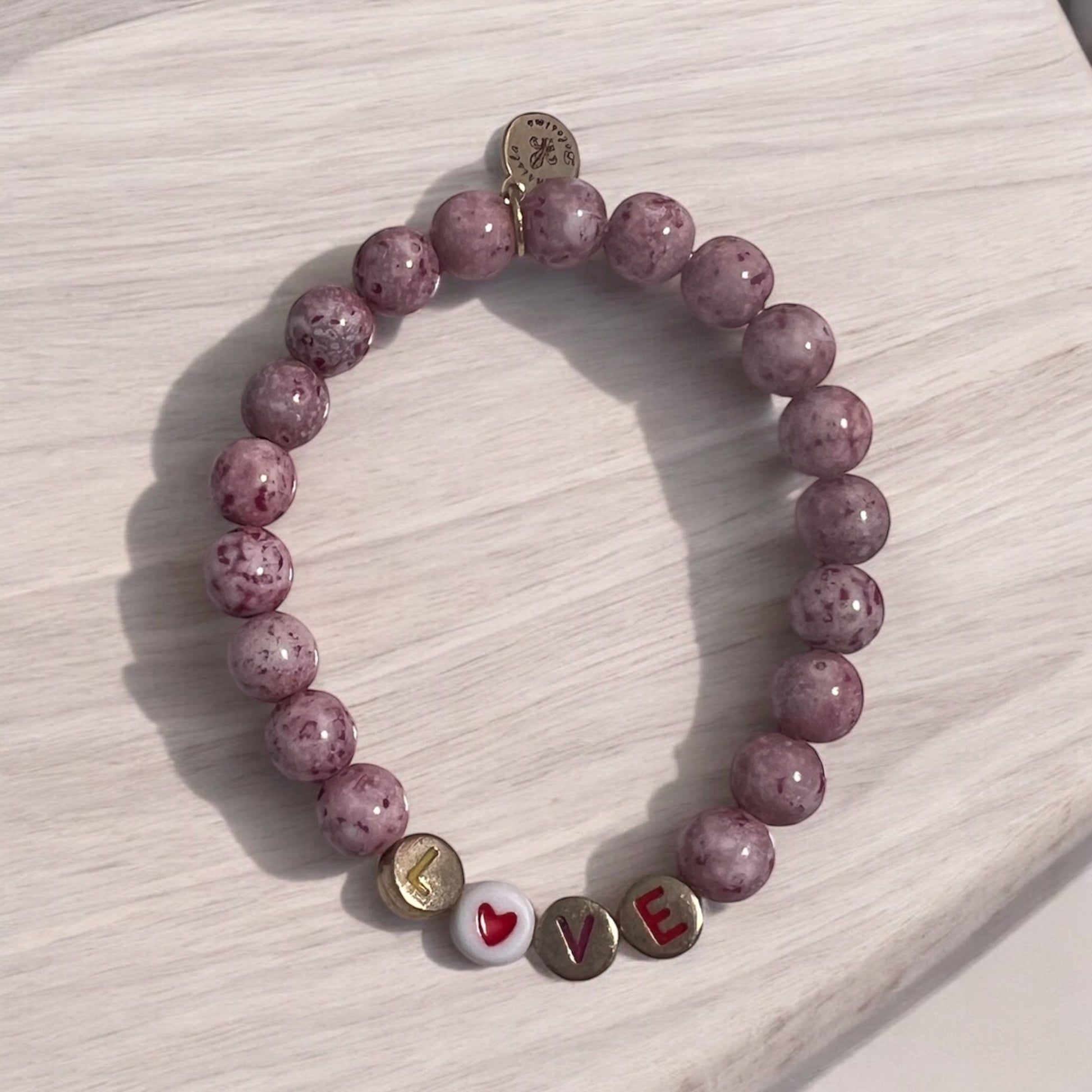 A pink beaded stretch bracelet with the word 'love' and a heart symbol on a wooden surface.