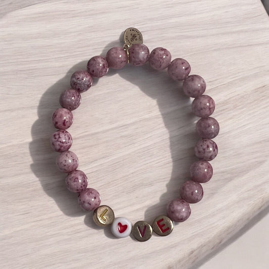 A pink beaded stretch bracelet with the word 'love' and a heart symbol on a wooden surface.