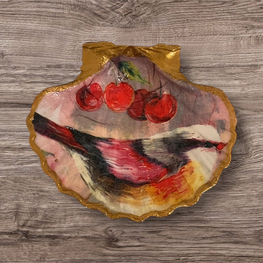 A decorative scallop shell with a painted red bird and cherries, with a gold edge.
