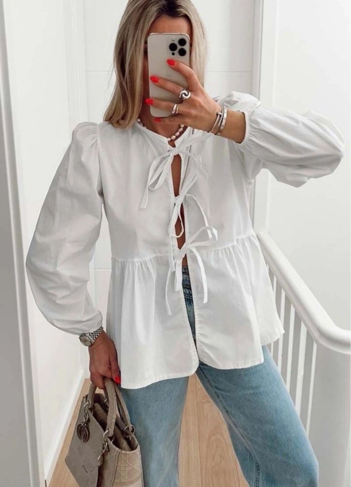 A person wearing a white long sleeve tie front top with jeans, taking a mirror selfie.